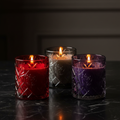 Three jewel-tone embossed glass soy candles on dark marble - hero shot