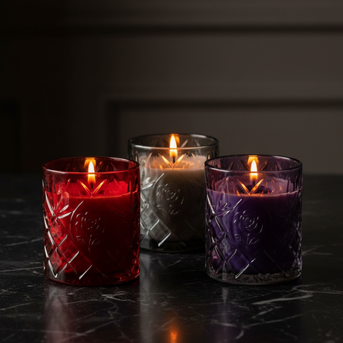 Three jewel-tone embossed glass soy candles on dark marble - hero shot